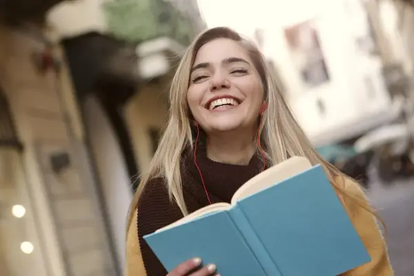 Uśmiechnięta dziewczyna z książką i słuchawkami na ulicy. Może to być studentka, która właśnie skończyła lekcje w szkole w Danii.