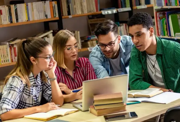 Studenci pochłonięci nauką historii przy laptopie w bibliotece.