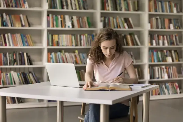 Młoda kobieta uczy się w bibliotece, zastanawiając się, czy studia chemiczne to dobry wybór.