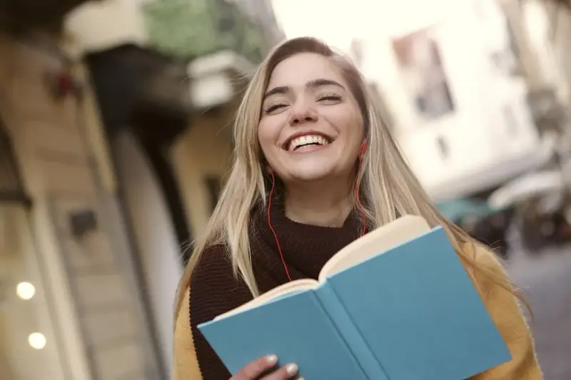 Uśmiechnięta dziewczyna z książką i słuchawkami na ulicy. Może to być studentka, która właśnie skończyła lekcje w szkole w Danii.